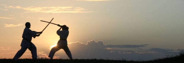 Two martial art practitioners sparring with wooden sticks at sunset