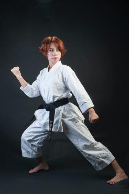 Woman practicing martial art in white gi with black belt in fighting stance