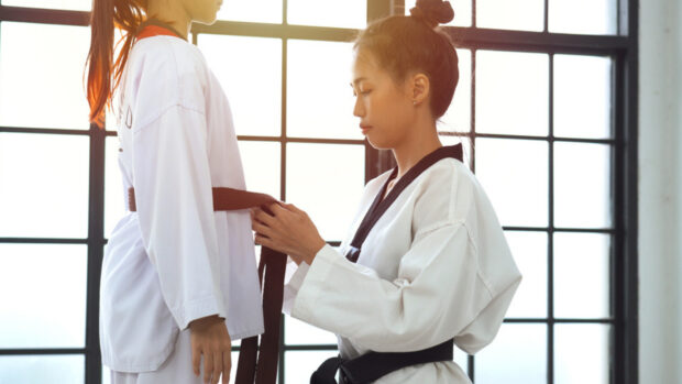 A martial art practitioner tying a brown belt on another in a bright training room
