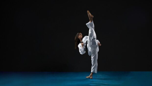 Woman practicing martial art high kick in white uniform on blue floor