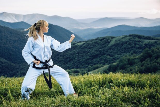 Woman practicing martial art in nature surrounded by mountains and green grass