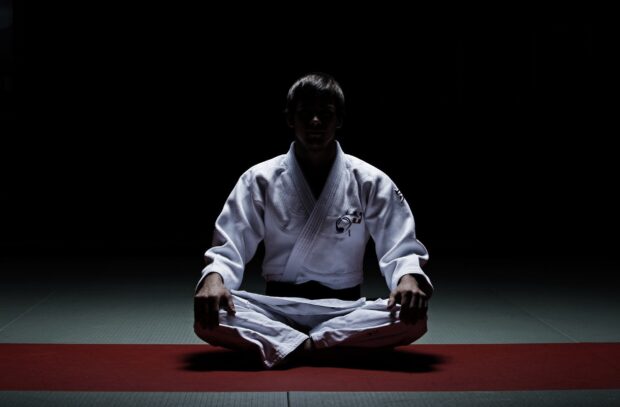 Martial artist sitting cross legged on mat in a dojo practicing martial art