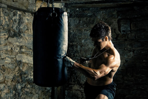 Muscular man practicing martial art training with punching bag in gym
