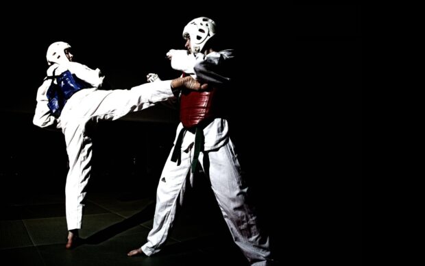 Two martial art practitioners sparring with protective gear in a dark studio