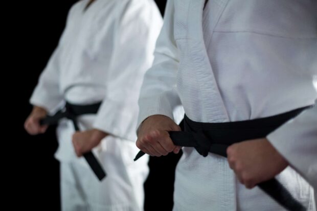 Two martial art practitioners tying black belts on their white uniforms