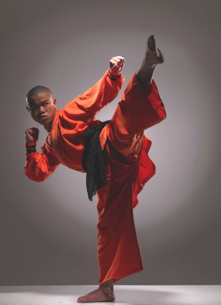 A martial art master performs a high kick in traditional orange attire