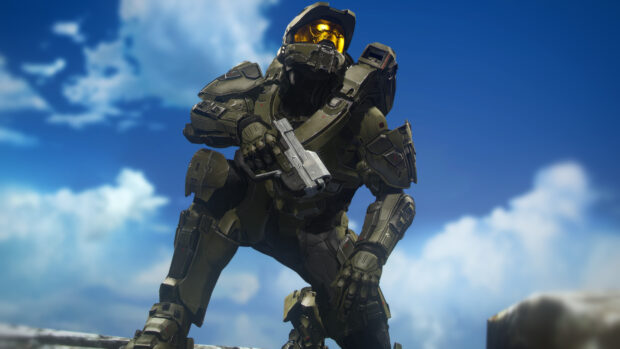 Master Chief kneeling in advanced armor holding a futuristic gun under a clear blue sky