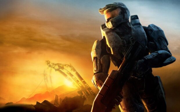 Master Chief stands ready with a futuristic weapon in a fiery sunset landscape