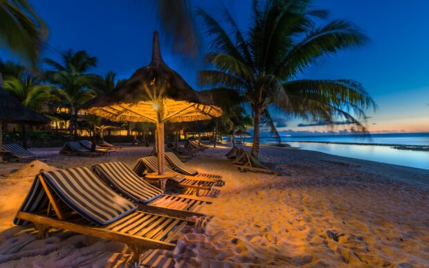 Relaxing Mauritius Island beach with striped lounge chairs and palm trees at dusk