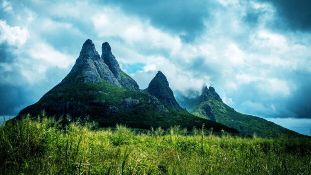 Lush mountains of Mauritius Island under cloudy sky with green grass in foreground