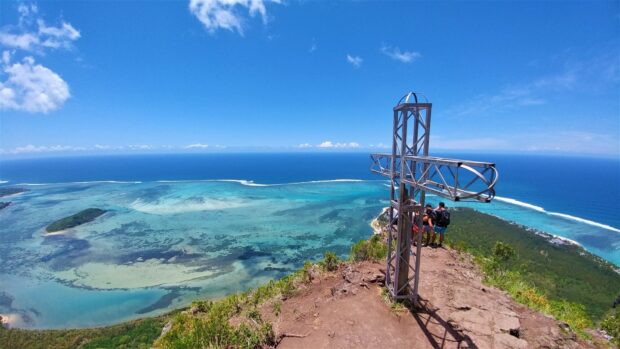 Scenic view of Mauritius Island coastline from mountain with hikers near metal cross