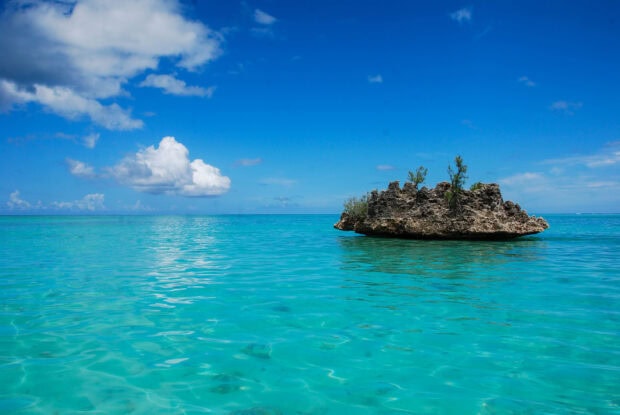 Clear turquoise sea around a rock formation in Mauritius Island with a bright blue sky and clouds