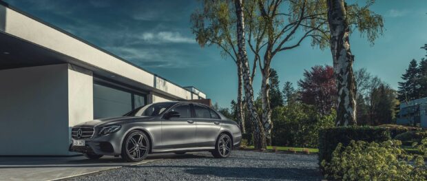 A Mercedes Benz car parked in front of a modern house surrounded by trees and greenery