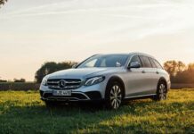 A silver Mercedes Benz parked in a green field during sunset with trees in the background