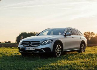 A silver Mercedes Benz parked in a green field during sunset with trees in the background