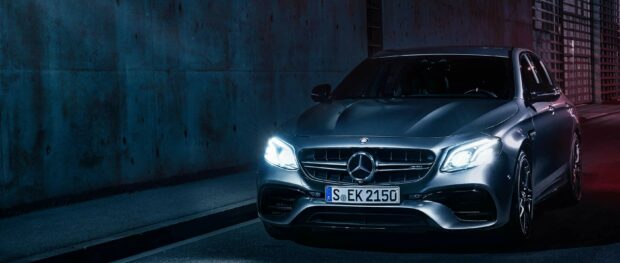 A sleek Mercedes Benz parked at night with headlights on against an urban backdrop