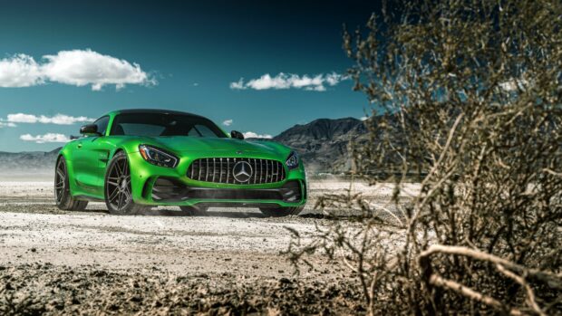 Green Mercedes Benz car driving on a dry desert road under a clear blue sky