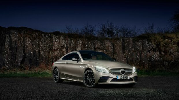 Silver Mercedes Benz car parked in front of rocky terrain at night with headlights on
