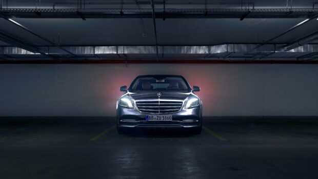 A Mercedes Benz car with headlights on parked in a dark underground garage