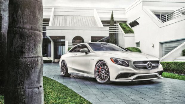 White Mercedes Benz coupe parked in front of a modern house with green bushes