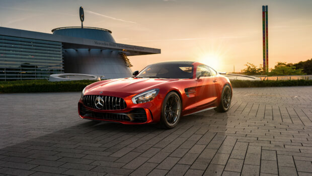 A red Mercedes Benz sports car parked outside the Mercedes Benz building at sunset with clear skies
