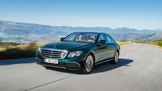 A Mercedes Benz car driving on a mountain road with clear blue sky and hills in the background
