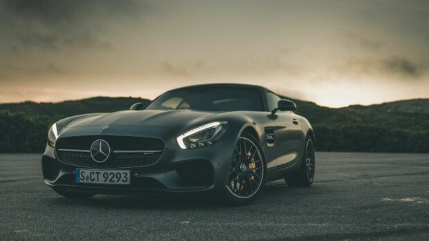 A sleek Mercedes Benz sports car parked on an asphalt road during sunset with illuminated headlights
