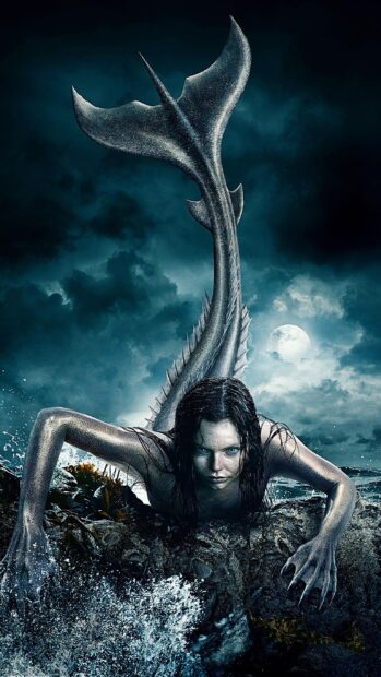 A fierce mermaid with a long tail emerging from the ocean under a cloudy night sky