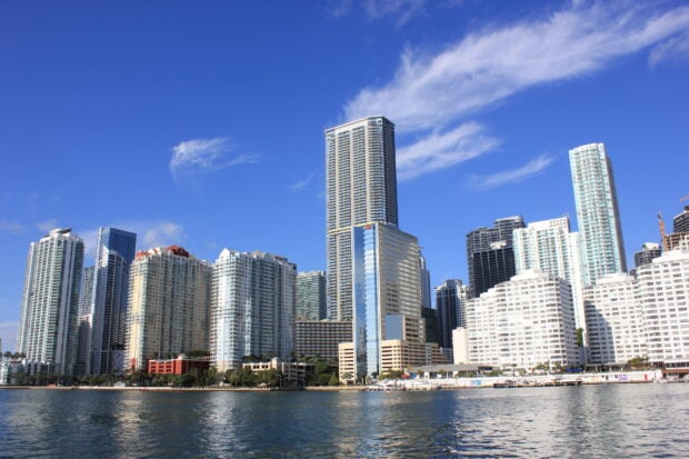 Miami Beach skyline with tall buildings under a clear blue sky reflecting on the water