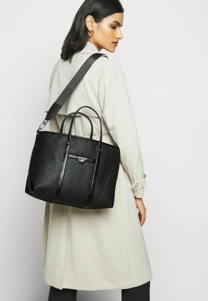 A woman wearing a light trench coat carrying a Michael Kors tote bag on her shoulder