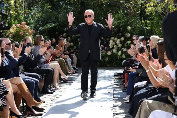Michael Kors walking on the runway greeting the applauding crowd at a fashion show outdoors