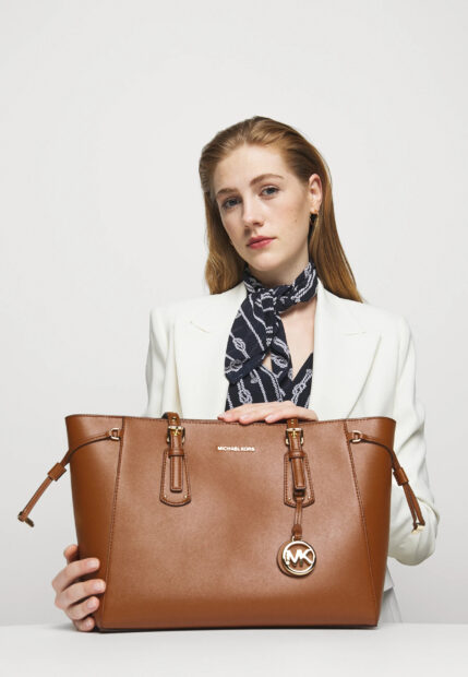 A woman holding a brown leather Michael Kors bag with a black and white scarf