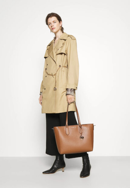 A woman wearing a beige trench coat and holding a Michael Kors handbag