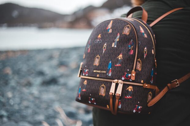 A close up of a Michael Kors backpack with colorful travel themed prints on the strap