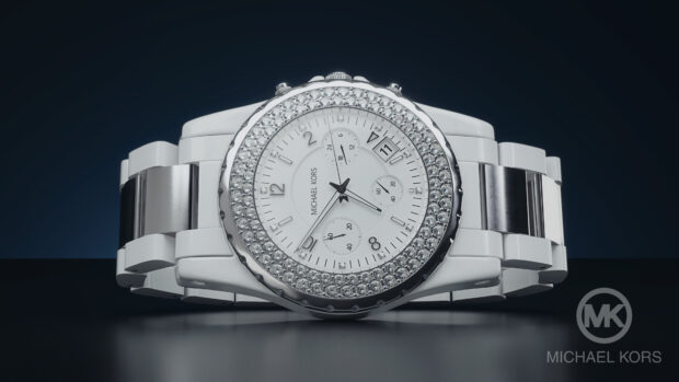 A white Michael Kors luxury watch with diamond bezel on a dark surface