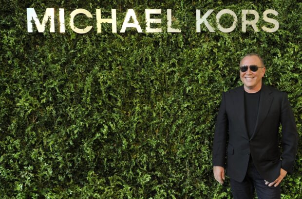 Michael Kors standing in front of a green wall displaying Michael Kors logo