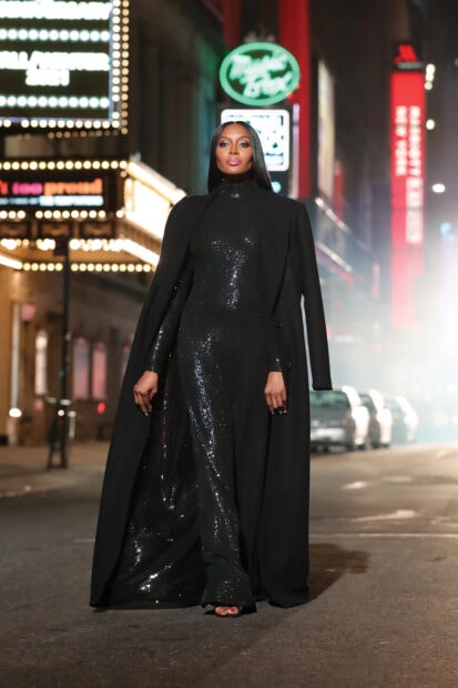 Woman wearing a black sequined dress and coat walking on a city street at night