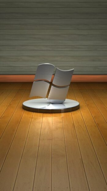 A metallic Microsoft logo displayed on a wooden floor with a wooden wall background