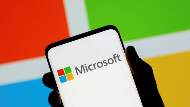 A hand holding a phone displaying the Microsoft logo on a colorful background