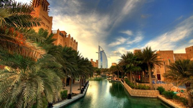 Traditional Middle East architecture alongside palm trees and a canal in a cityscape