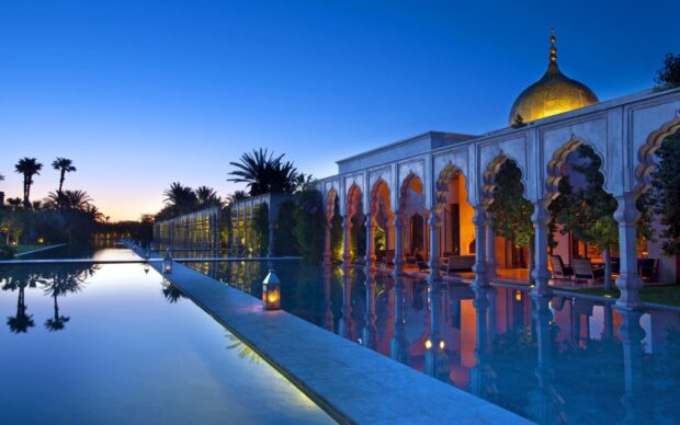 Middle East architecture reflecting on a calm pool at sunset with palm trees and a golden dome
