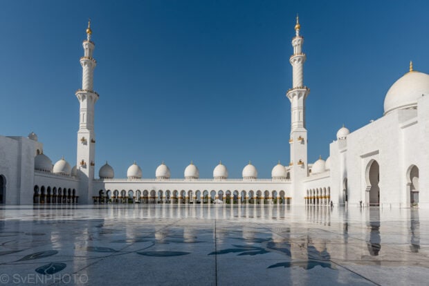 The grand mosque courtyard in Middle East with white domes and tall minarets under clear blue sky