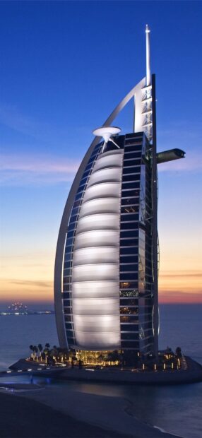 Iconic Middle East architecture with illuminated sail shaped building at sunset