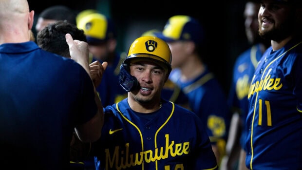 Milwaukee Brewers player wearing a yellow helmet and navy blue uniform celebrating with teammates in the dugout