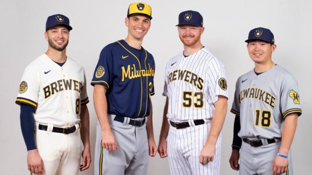Four Milwaukee Brewers players wearing different team uniforms standing together smiling