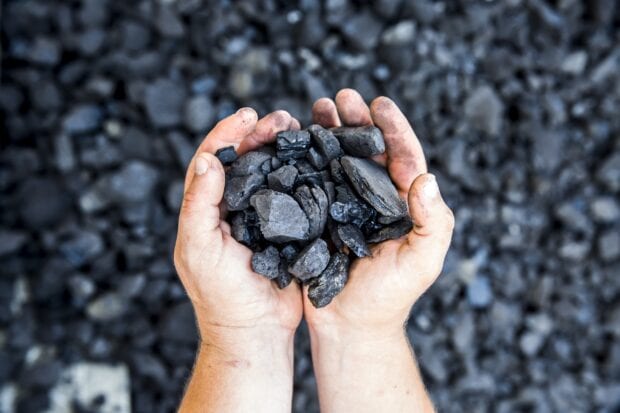 Hands holding black minerals on a rocky surface showing natural minerals