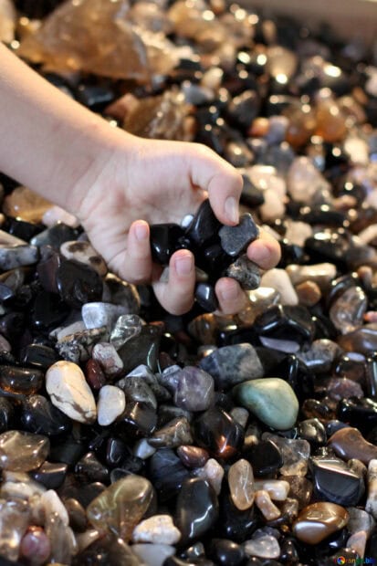 A hand holding various polished minerals among a collection of colorful minerals