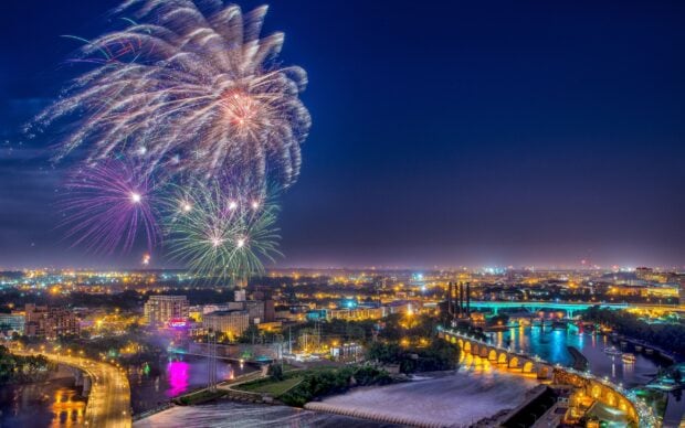 Fireworks light up the sky over Minneapolis cityscape with river and bridges at night