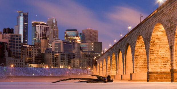 Historic stone arch bridge lit up at dusk near Minneapolis skyline