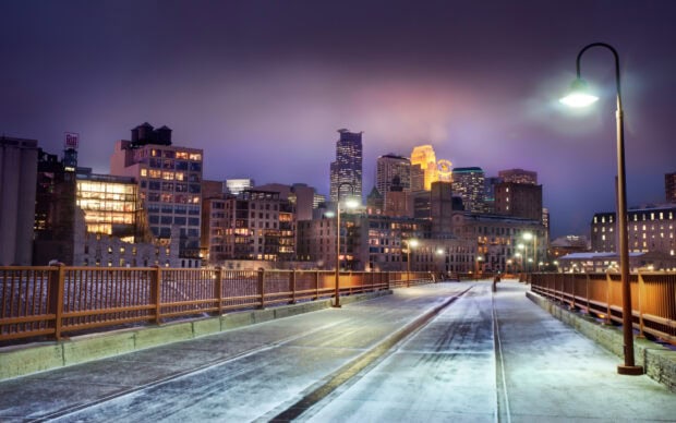 Minneapolis city skyline with lit buildings behind a snowy bridge at dusk
